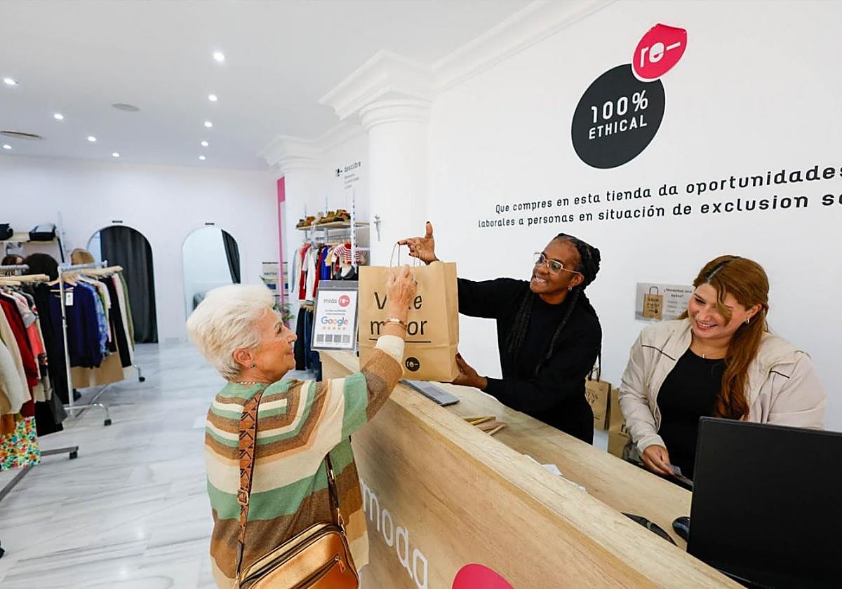 Una clienta de la tienda Moda Re- es atendida por Anna y Yennediey, beneficiarias del proyecto de inserción de Cáritas.