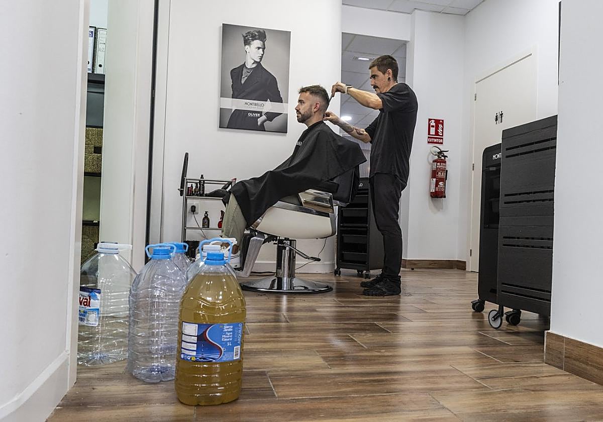 Imanol Oliver, ayer atendiendo a un cliente en la Peluquería Oliver, en Los Alcázares. En primer plano, varias botellas.
