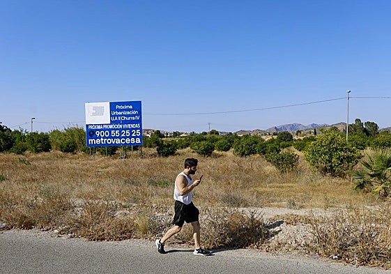 Un hombre camina junto a unas parcelas en el municipio de Murcia, en las que se anuncia la construcción de un residencial.