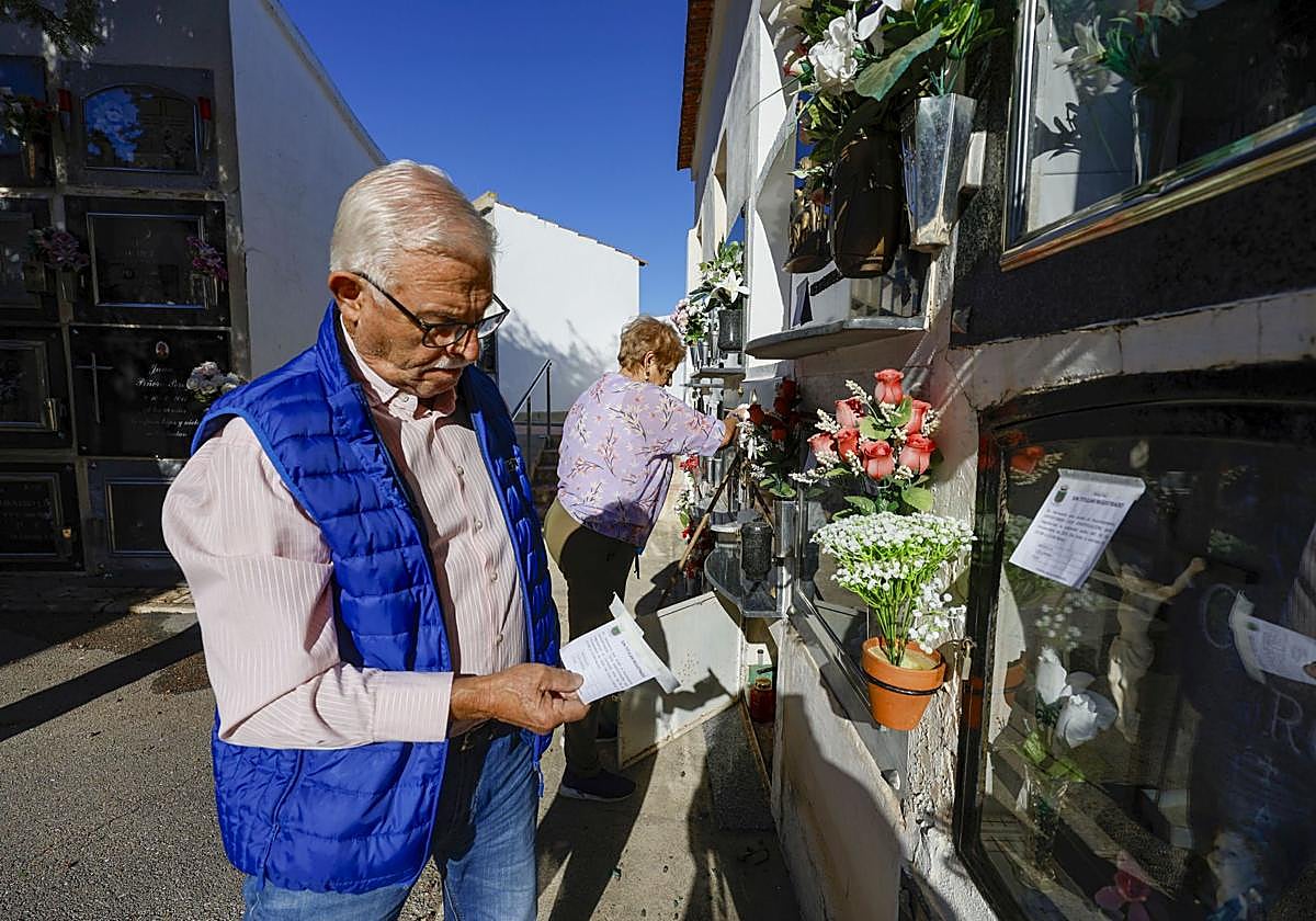 Dos vecinos de Ceutí limpian tumbas de familiares, con el cartel del Ayuntamiento en la mano.
