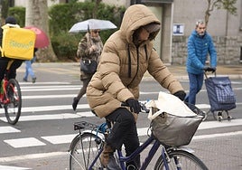Una mujer circula en bicicleta con la capucha del abrigo puesta para protegerse del viento.