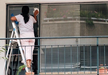 Una trabajadora del hogar limpia los cristales en una vivienda.