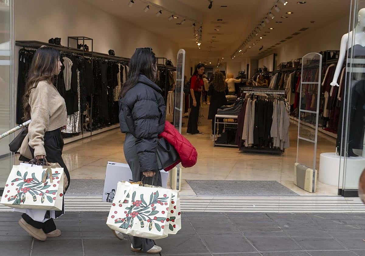 Dos jóvenes con bolsas de regalos pasan frente a una de las tiendas del centro de la ciudad.