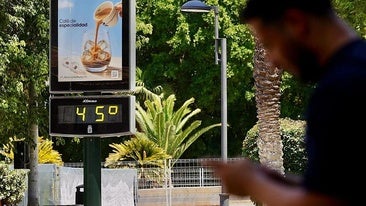 Un hombre consulta su teléfono en Murcia junto a uno de los termómetros de la ciudad.