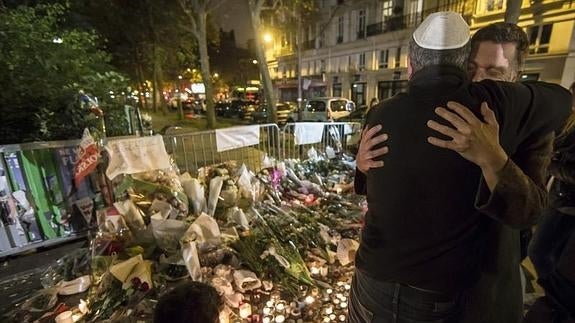 Dos personas se abrazan ante multitud de velas y flores depositadas en las cercanías de Bataclan. 