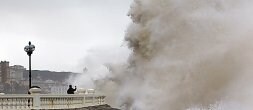 Un osado viandante fotografía una gigantesca ola rompiendo contra las rocas en San Sebastián. / EFE