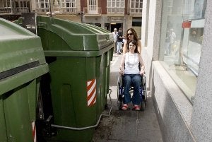 Julia y una persona de apoyo intenta pasar por una acera de la calle Jara, entre contenedores de basura y la pared. / JOSÉ ALBALADEJO