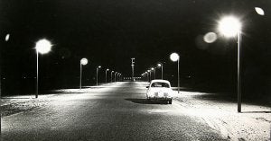 Un coche, de noche por lo que hace medio siglo era la Gran Vía de La Manga, una carretera con dos hileras de farolas. ::                             ANTONIO SOLANO