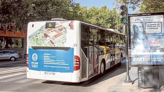 Un autobús con publicidad de la UCAM pasa frente a un expositor con un anuncio de ISEN, ayer en el Paseo de Alfonso XIII.