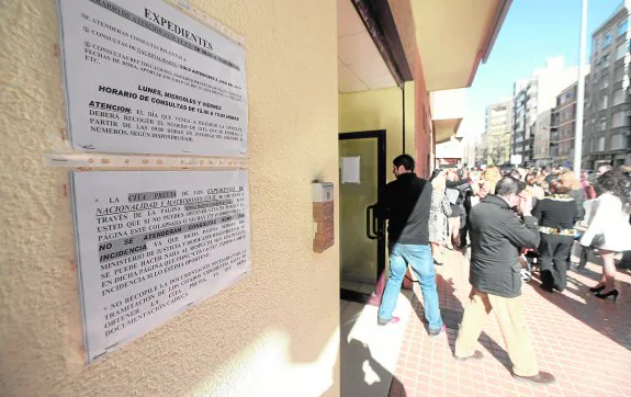Usuarios del Registro Civil de Cartagena, junto a carteles con advertencias sobre los problemas con la cita previa por internet.