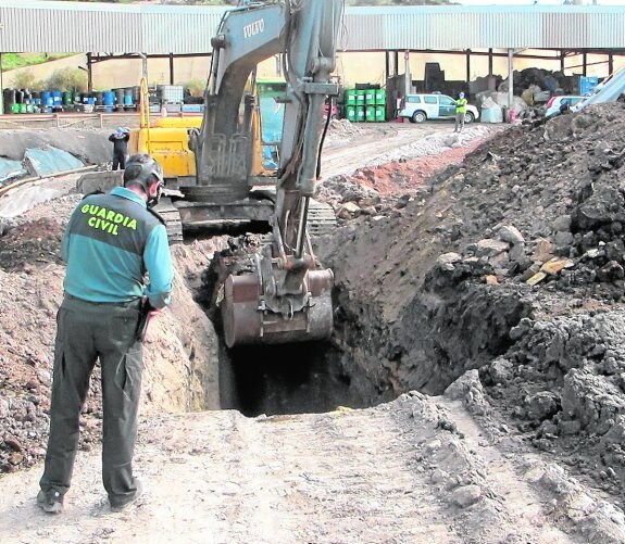 Un guardia supervisa la extracción de residuos con una excavadora en el vertedero industrial. 