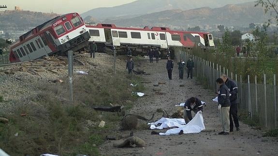 Un hombre cubre uno de los cadáveres del accidente ocurrido en Lorca en 2001; al fondo, el tren descarrilado. 