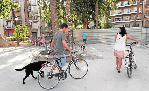 Vecinos y transeúntes cruzan la plaza dominada ahora por las vallas metálicas que protegen la zona arqueológica.