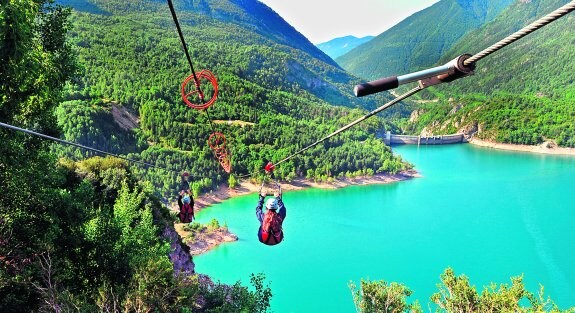 Dos personas descienden por la tirolina sobrevolando las aguas del pantano de Búbal, en el aragonés Valle de Tena. 