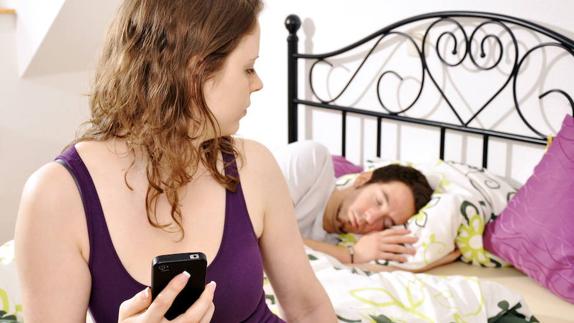 Una mujer revisa su teléfono mientras su pareja duerme. 