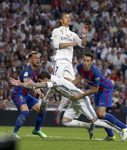 El defensa del Real Madrid, Sergio Ramos (2d), cae ante el jugador del FC Barcelona, Sergio Busquets, durante el encuentro correspondiente a la jornada 33 de primera división