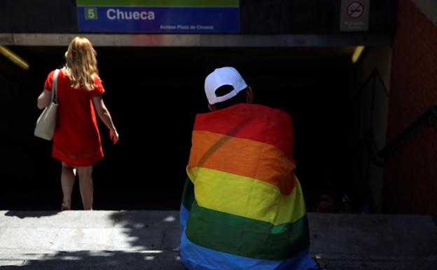 Un hombre ataviado con la bandera LGTB junto al acceso de Metro de Chueca.