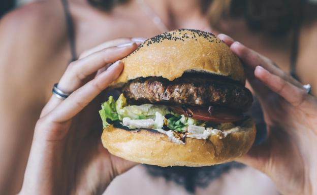 Una mujer, comiendo una hamburguesa.