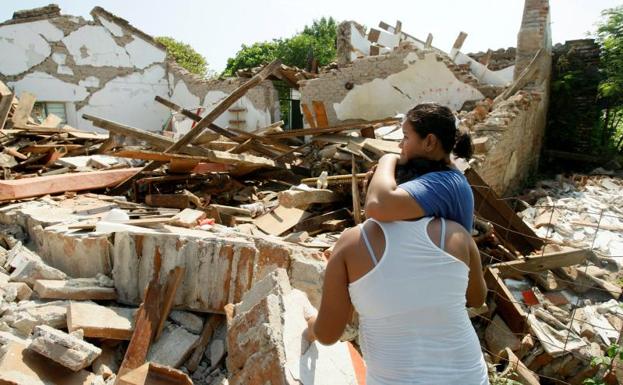Dos mujeres se abrazan frente a su vivienda destrozada.