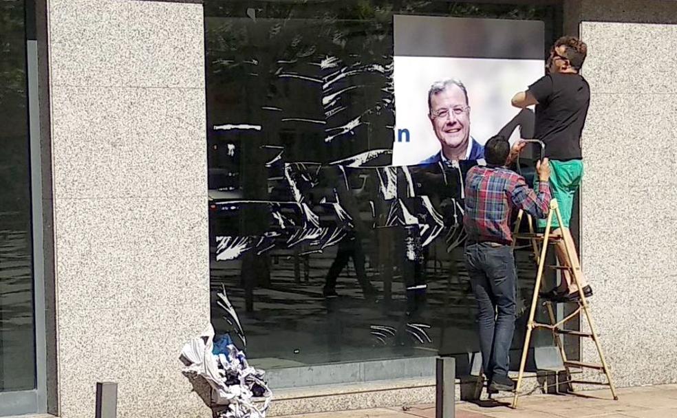 Dos operarios retiran la imagen de Antonio Silván de la sede electoral del PP municipal en la Plaza de las Cortes de la capital.