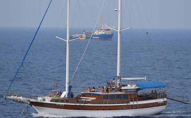 Un barco turístico pasa por delanter del bardo de búsqueda y rescate Sea-Watch 3, que permanece bloqueado cerca de la isla de Lampedusa, Italia.