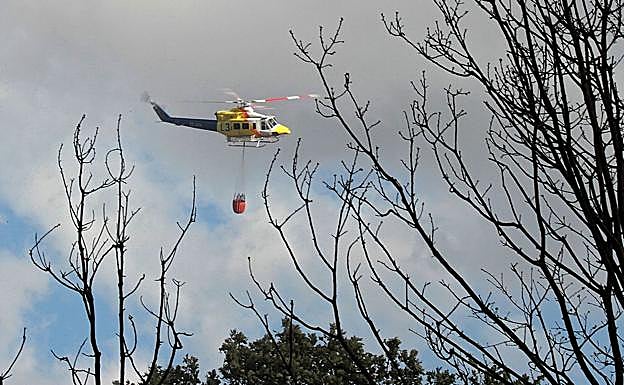 Imagen principal - Brigadistas y helicópteros trabajando en la zona del incendio.