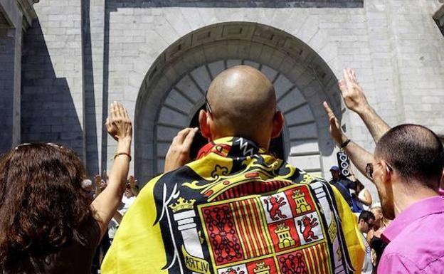 Varias personas saludan con el brazo en alto frente a la basílica del Valle de los Caídos.