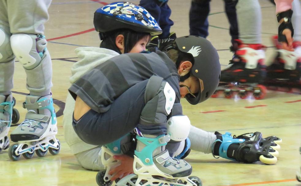 Dos niños tratan de levantarse con sus patinetes.