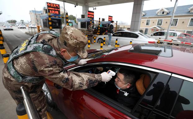 Un miembro del Ejército controla la temperatura corporal de un conductor en el peaje de una autopista en Wuhan.