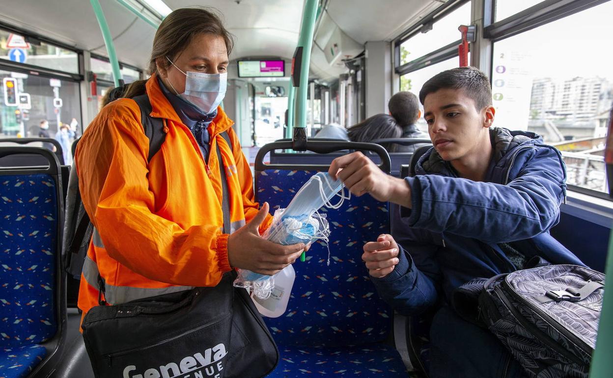 Una empleada del transporte público en Ginebra reparte mascarillas a los usuarios de un autobús.