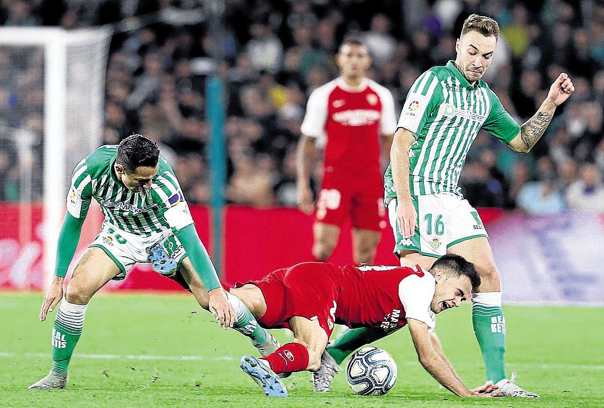 El defensa del Sevilla FC Sergio Reguilón (c), cae entre Loren Morón (d) y el mexicano Andrés Guardado (i) del Betis.