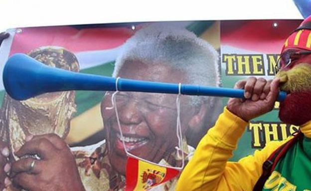 Un aficionado sopla la vuvuzela junto a una imagen de Nelson Mandela 