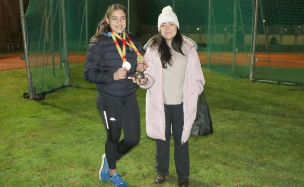 Galería. Fiona Villarroel y Margarita Ramos posan con un peso y las dos medallas de oro logradas por la primera en los campeonatos de España de atletismo sub-16 de este año 2020.