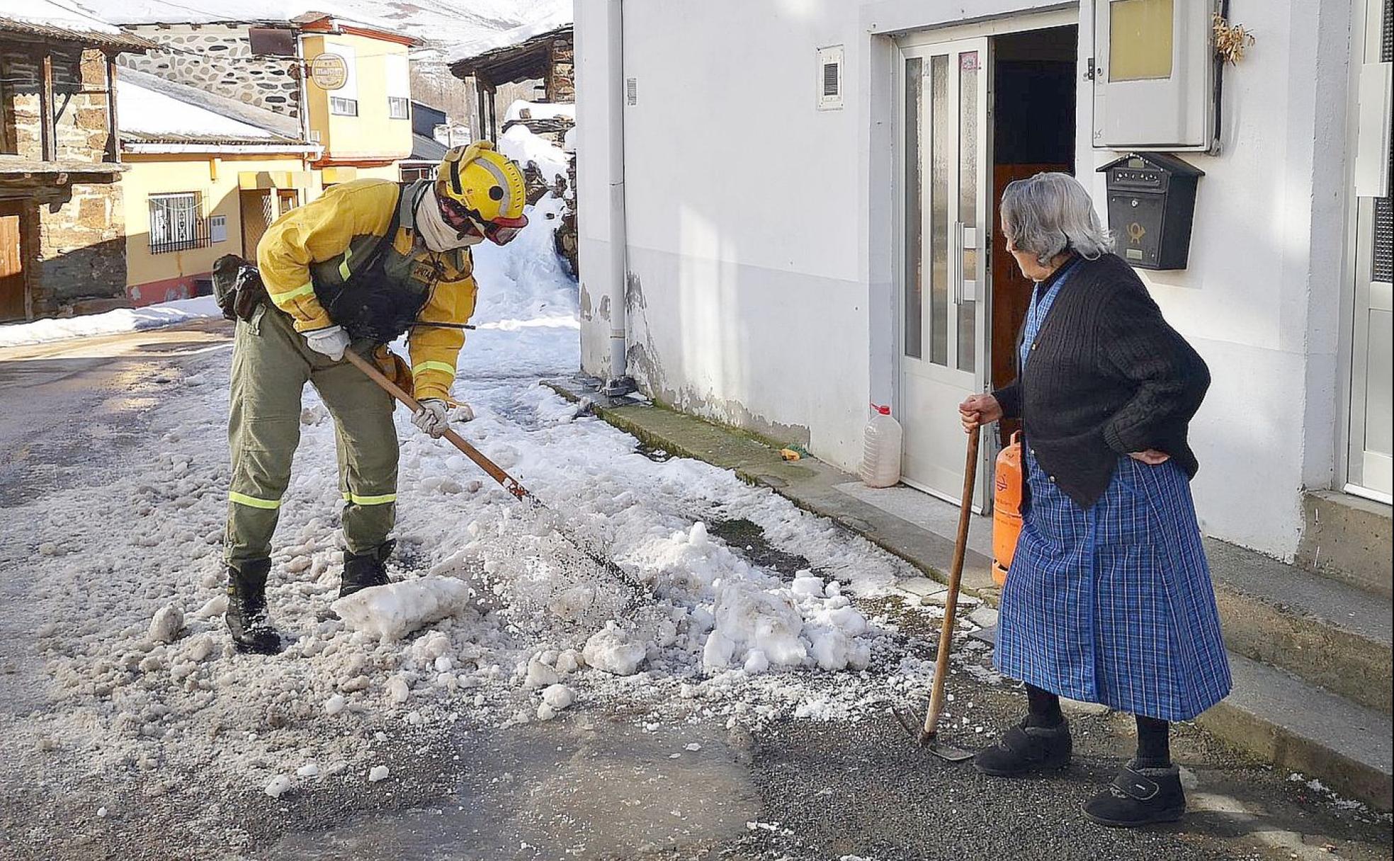 Un brigadista elimina el hielo ante la mirada de una vecina pertrechada con una azada. 