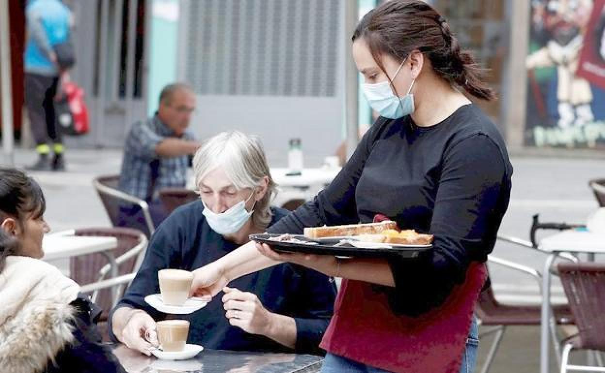 Una mujer atiende en una terraza a dos clientas.