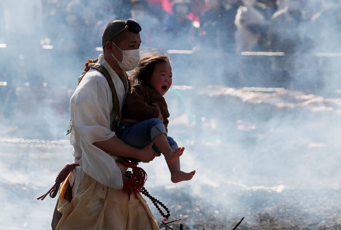 Un monje budista con una máscara protectora lleva a un niño mientras camina sobre carbones humeantes en el festival de caminar sobre el fuego, llamado hiwatari matsuri, en japonés, en el monte Takao en Tokio.