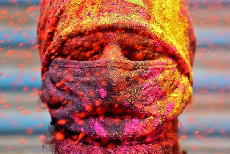 Un hombre que usa una mascarilla protectora reacciona cuando se le arroja polvo de color durante las celebraciones de Holi en Chennai, India.