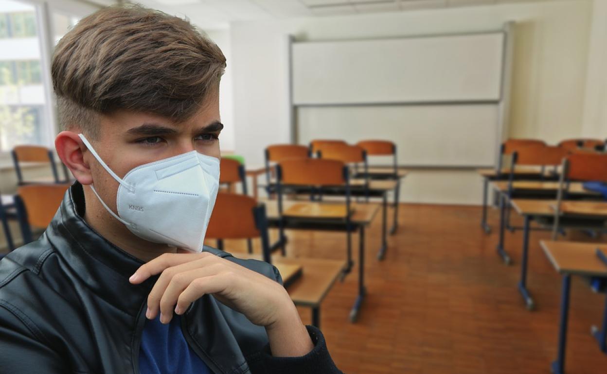 Un alumno, con su mascarilla, con un aula de fondo.