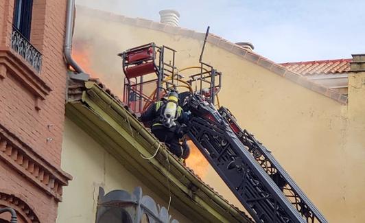 Los bomberos actúan en la techumbre del edificio incendiado.