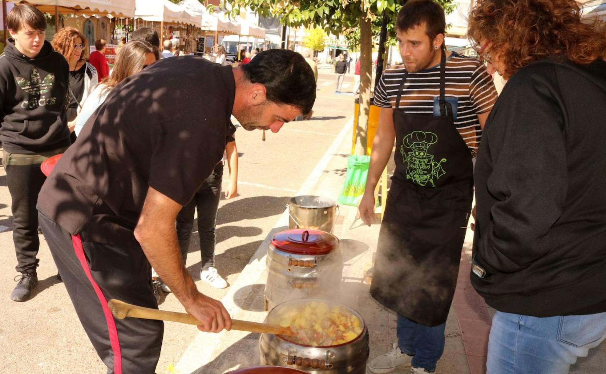 Un cocinero añade la carne a la olla ferroviaria ante la mirada curiosa de vecinos y visitantes.