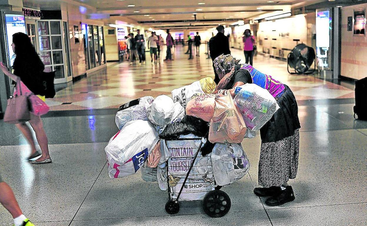 Una sintecho camina empujando un carro con sus pertenencias por los pasillos de una estación de Manhattan.