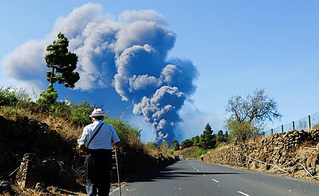 Un hombre camina mientras al fondo se vislumbra la columna de humo y cenizas. 