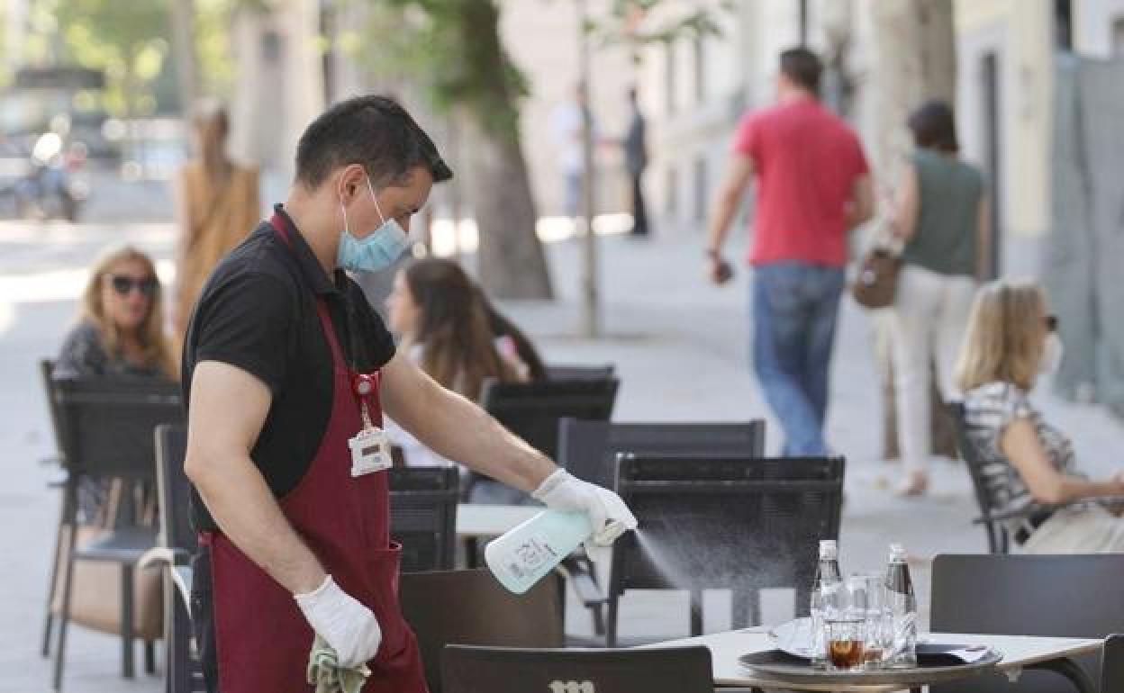 Imagen de un camarero desinfectando una mesa de una terraza durante la pandemia.