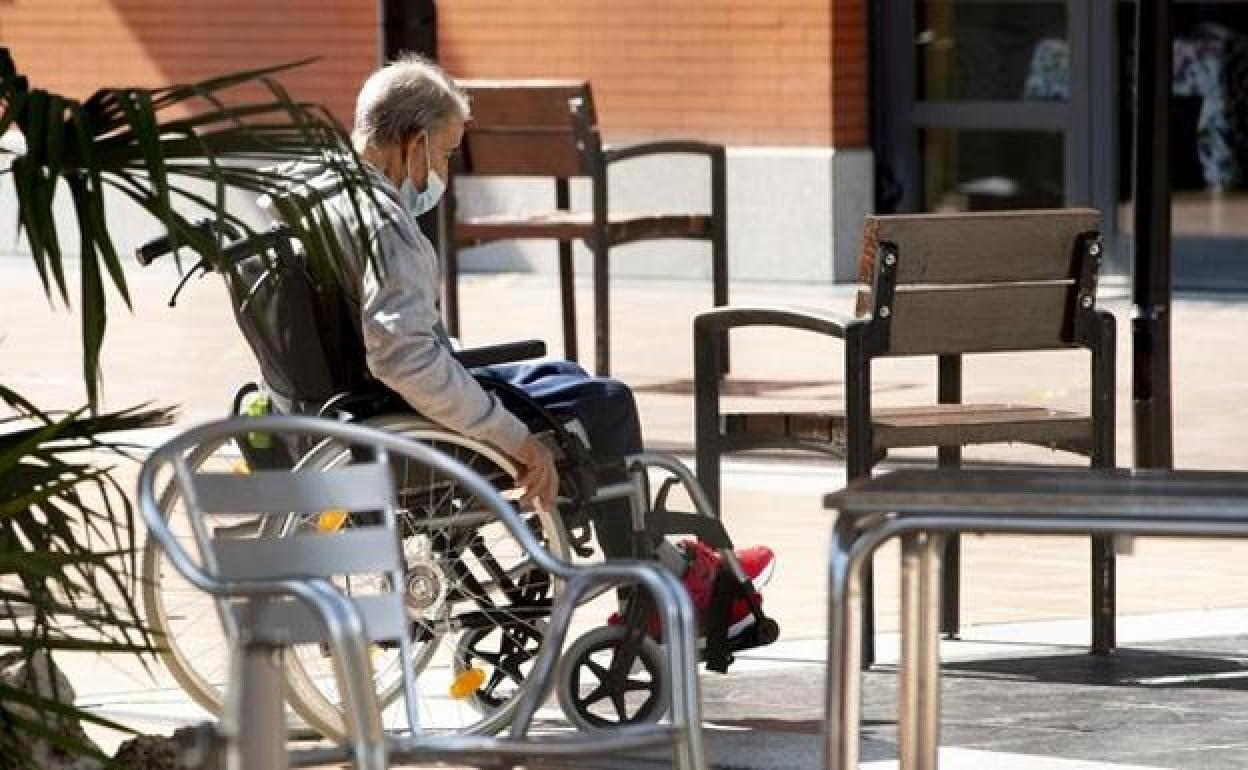 Un hombre en silla de ruedas en el patio de una residencia de mayores durante la pandemia.