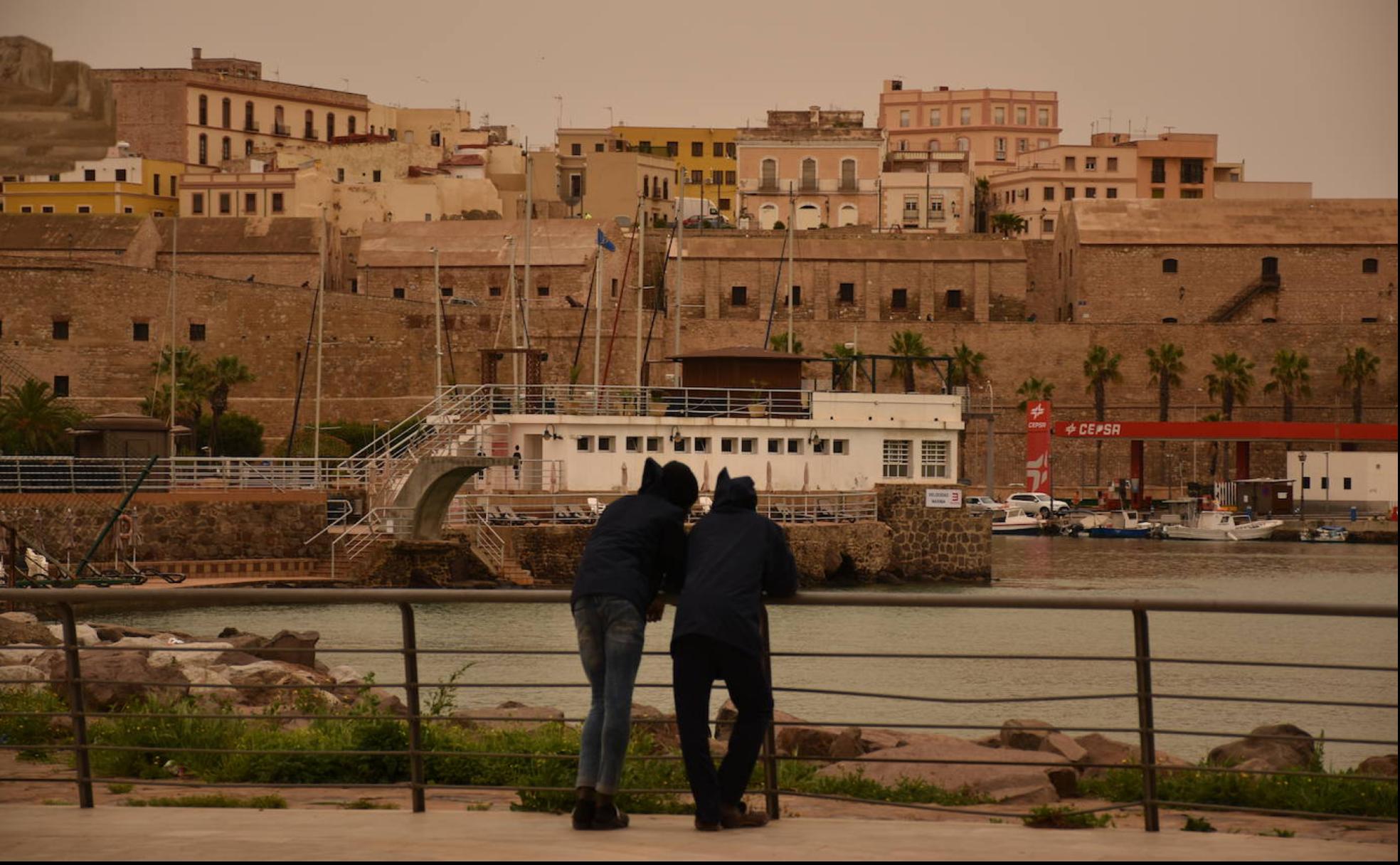 Dos jóvenes se apoyan en la barandilla dela Plaza del Mar, un mirador con vistas hacia el puerto, mientras la calima va cubriendo la ciudad.