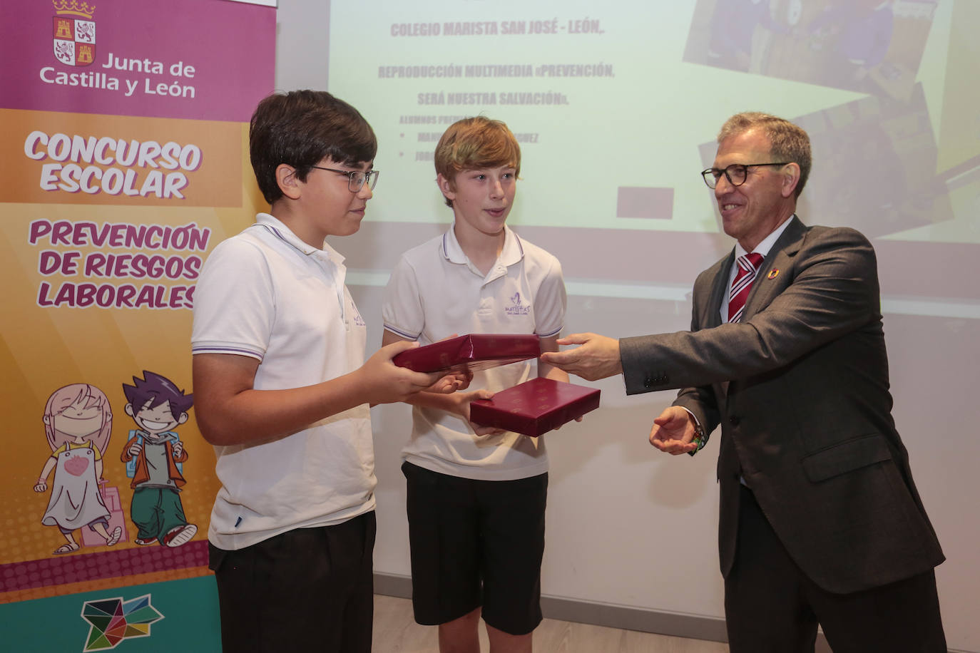 El consejero de Industria, Comercio y Empleo, Mariano Veganzones, entrega a los alumnos de primaria Manuel Cortés y Jorge González de Paz de este colegio leonés el galardón por su vídeo en el que repasan la importancia de prevenir en el colegio yen el trabajo para mejorar la seguridad.