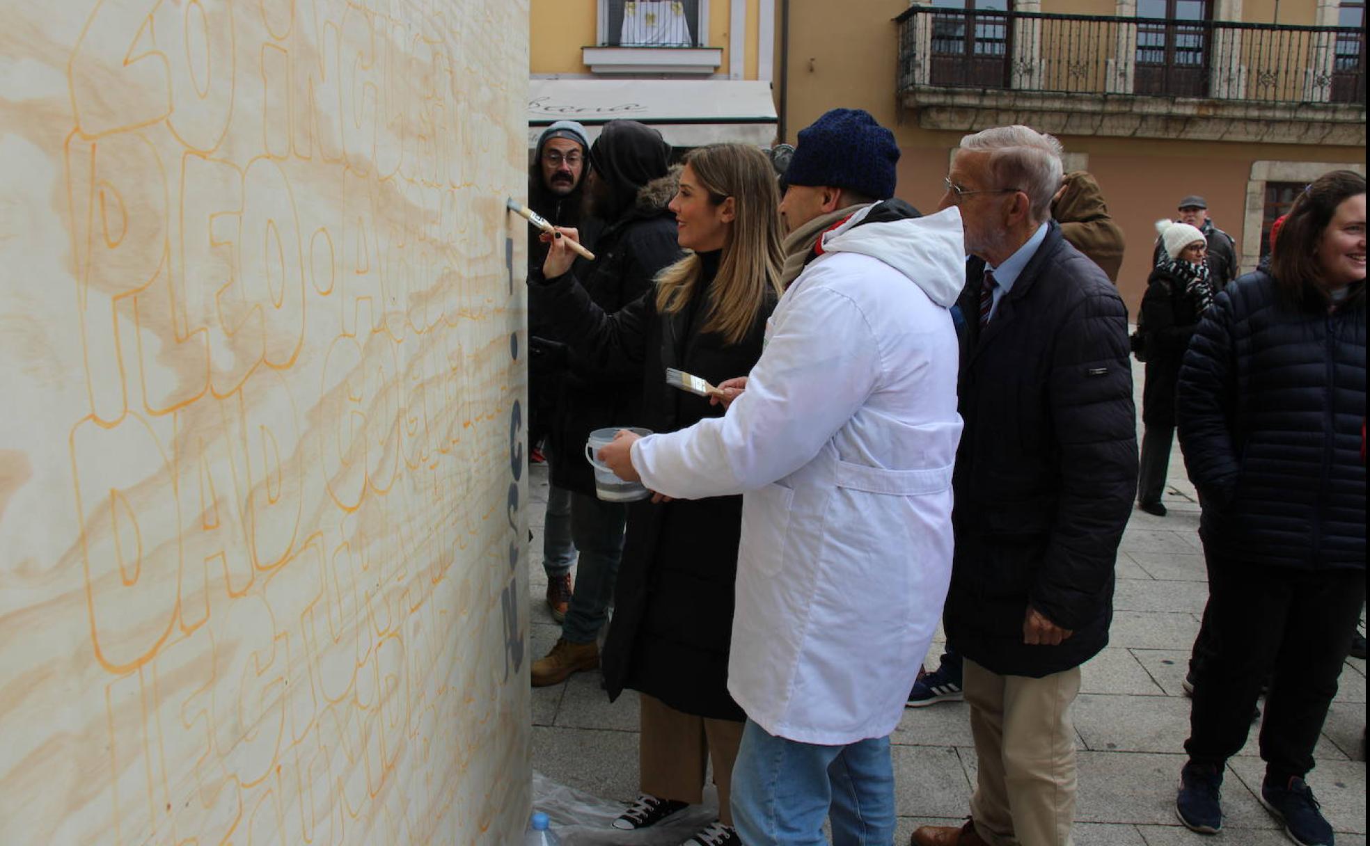 Uno de los miembros de la asociación rotula varios de los eslóganes del mural junto a la edil de Fiestas y el portavoz municipal del PRB.