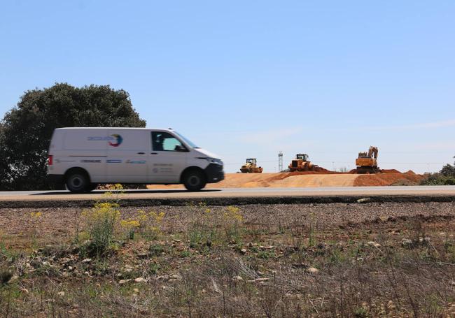 Una furgoneta circula por la N-120 y al fondo se pueden ver las máquinas de la obra.