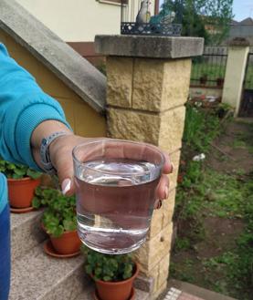 Imagen secundaria 2 - En la imagen de arriba y el centro, estado del agua en Pedrún el pasado domingo 4 de junio, según el Ayuntamiento; en la imagen de abajo, una vecina de Pedrún de Torío sostiene un vaso de agua del grifo.