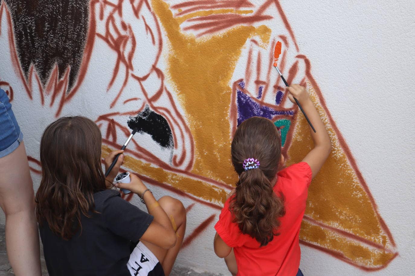 Dos niñas disfrutan pintando con su pincel el mural